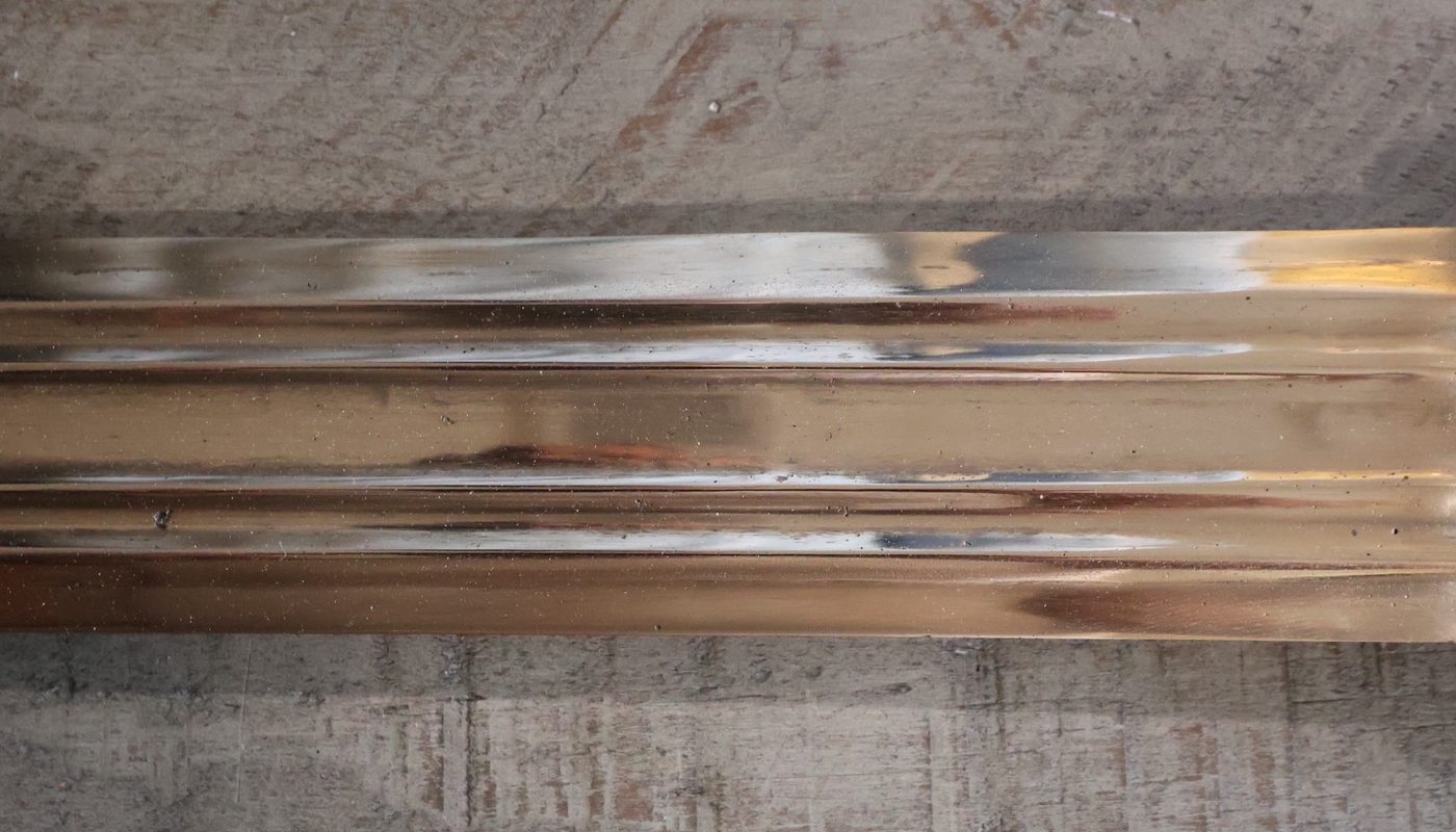 Mid-blade, filling the frame: parallel fullers cut the length of the polished bronze, catching the light in long bands