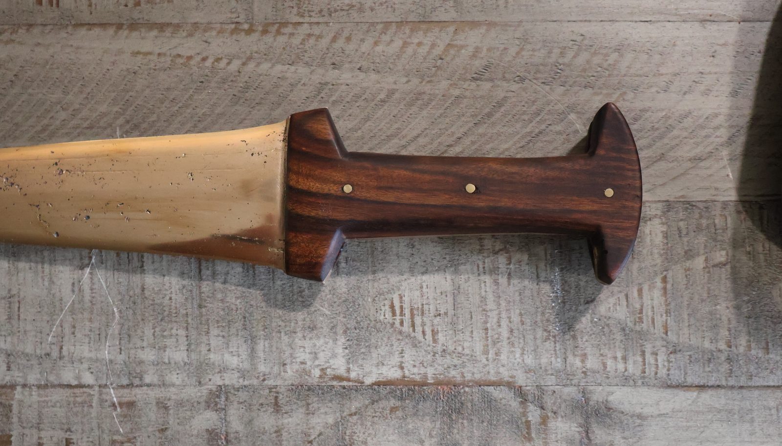 Where the bronze blade meets the wooden grip, the wood closing over the blade shoulders