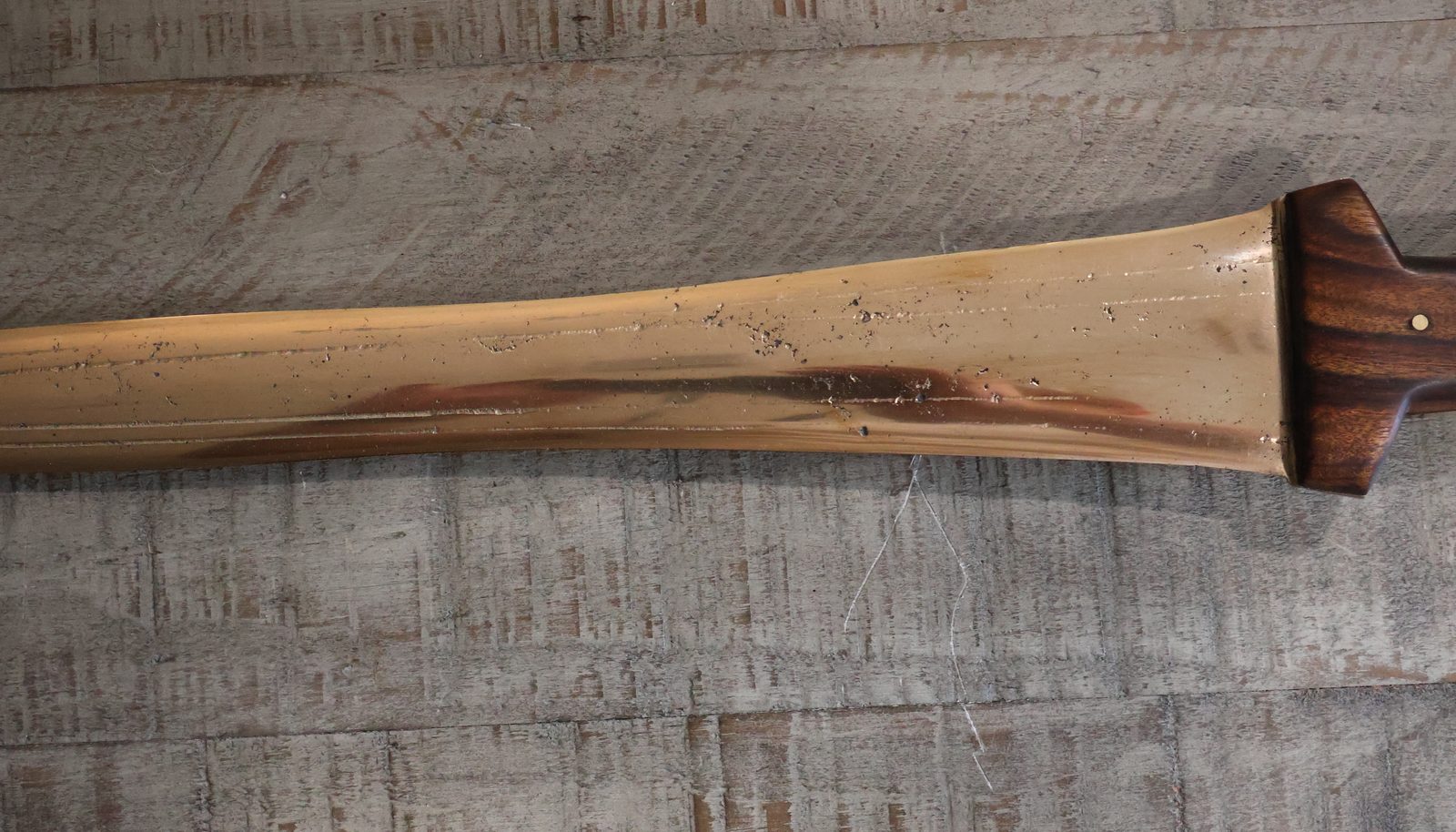 The blade running away from the handle, dark casting bands showing through the polished bronze